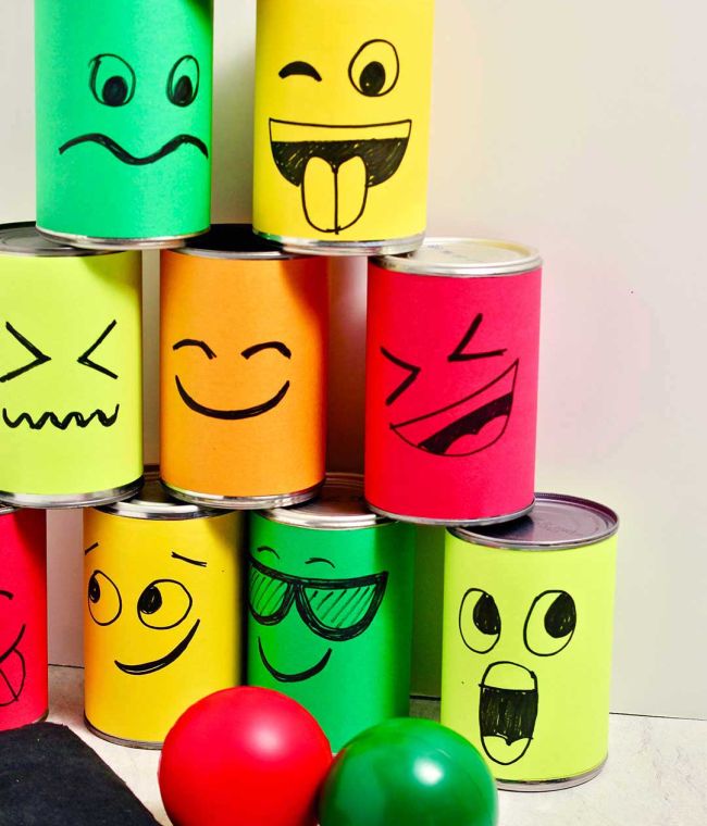 Pyramid of tin cans with colorful funny faces, next to three rubber balls