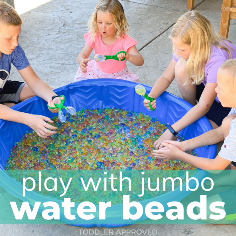 Several kids sit outside a blue kiddie pool that is filled with brightly colored water beads.